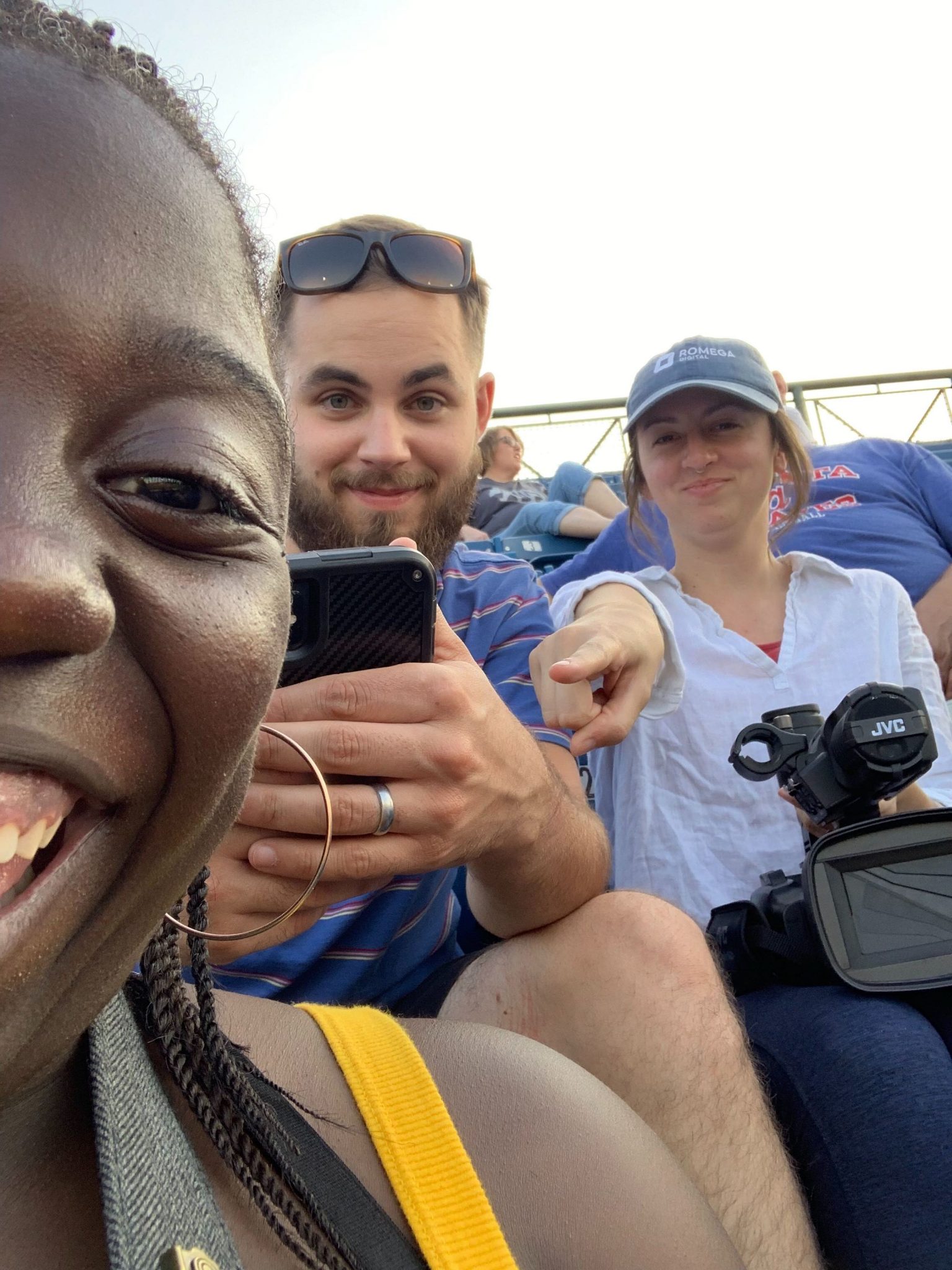 Two girls and a boy take a selfie in the stands at a baseball game.