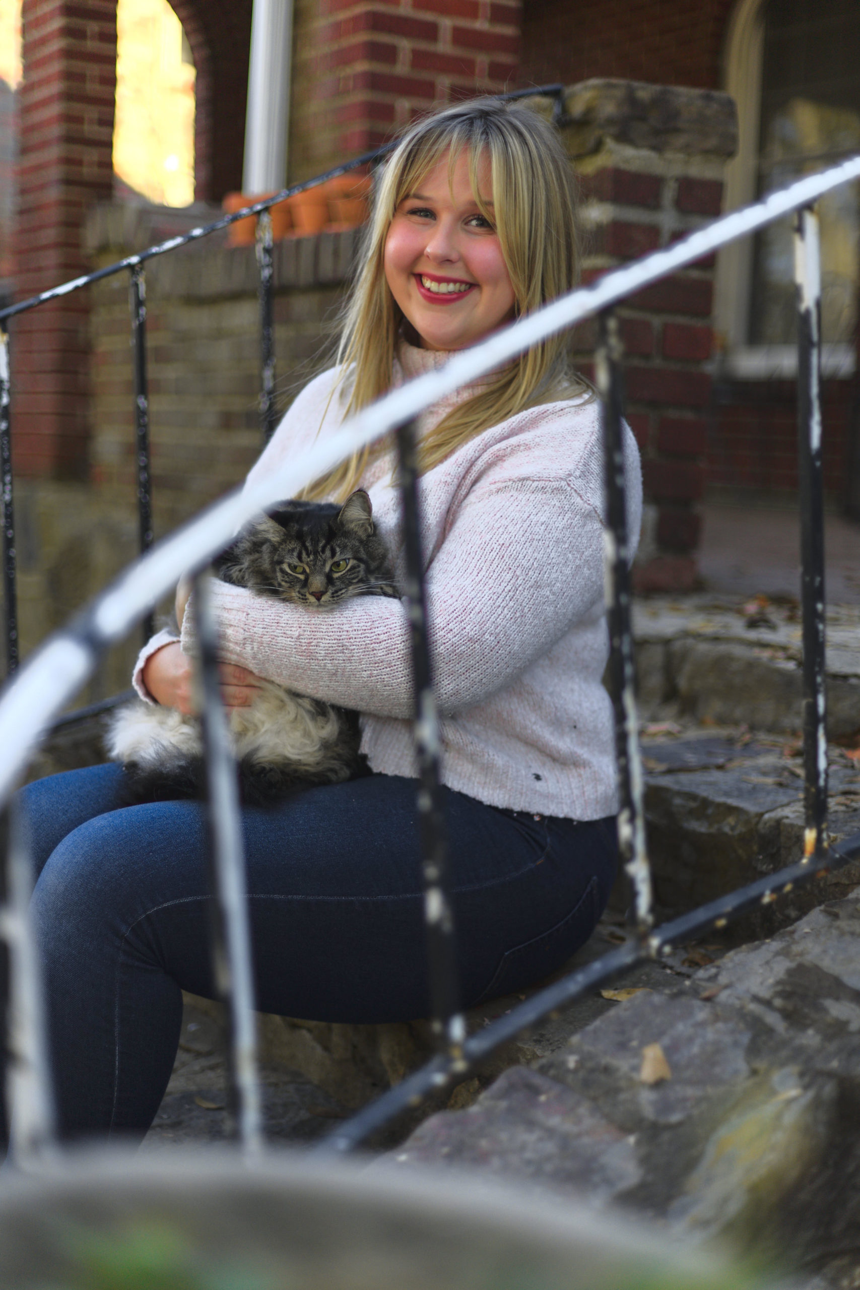 Anna sits on a set of stairs with her cat Franny, a longhaired tabby. 