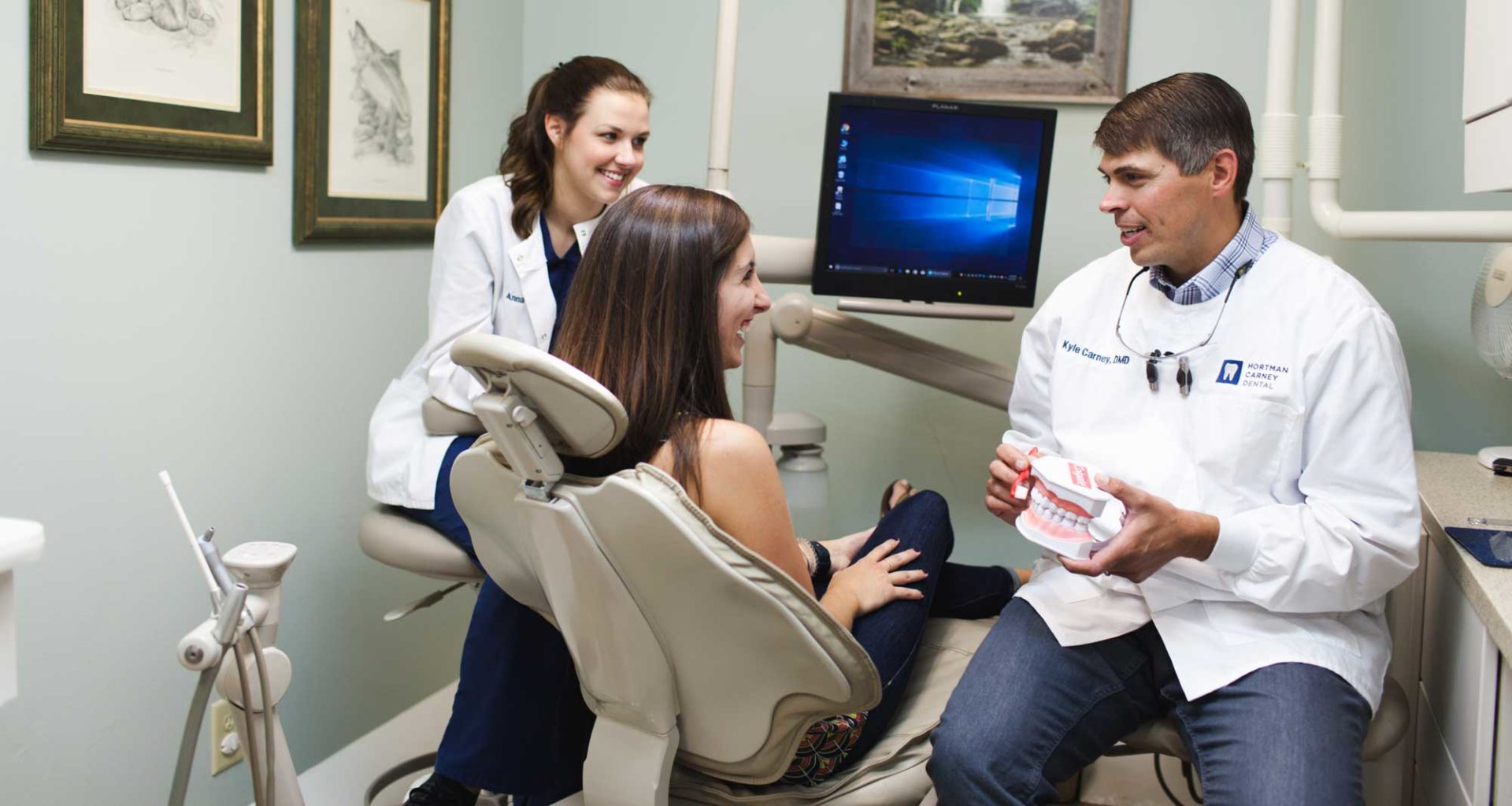 A dentist and assistant talk to a patient at the dental office